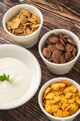 Assorted cereals with yogurt and milk on rustic wooden table