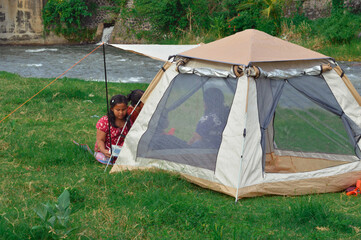 Two mothers and their children sit near the tent, enjoying lunch together on the grass beside the calm river