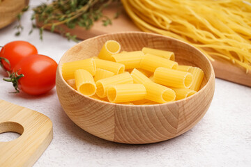 Wooden bowl with uncooked penne pasta and tomatoes on light background, closeup