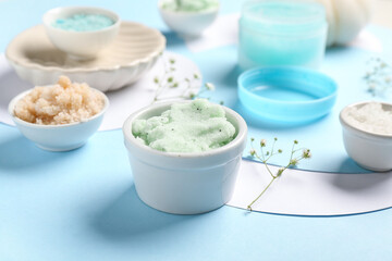 Bowls with scrub and flowers on blue background, closeup. Body massage concept