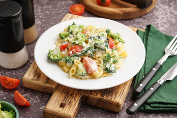 Plate of tasty pasta with broccoli and tomatoes on grunge grey background
