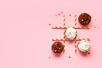 Tic tac toe game with tasty cupcakes and straws for Valentine's Day on pink background