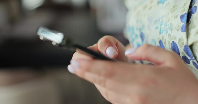 Close-up of hands of woman writes a text message on smartphone in the living room at home. Online shopping in social media.