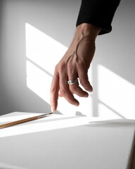 Fototapeta premium Creative Burnout / Blocked Flow. A hand hesitates above a blank page, representing creative struggle, burnout, and the vulnerability of artistic expression.