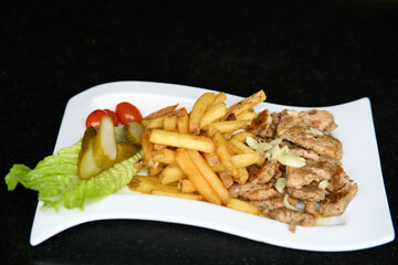Grilled chicken meat with french fries, pickles, tomatoes and salad on white plate