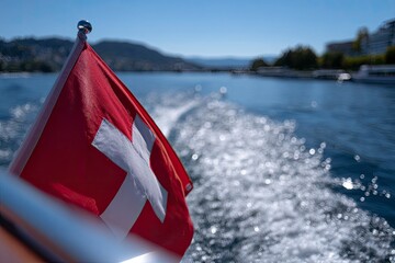 A Swiss flag on a boat waving against a backdrop of blue water  distant hills Focus on the flag