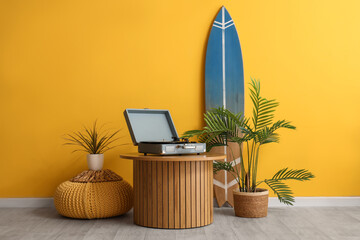 Coffee table, record player, houseplants and surf board near yellow wall in room