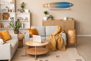 Interior of modern living room with laptop on coffee table and surfboard