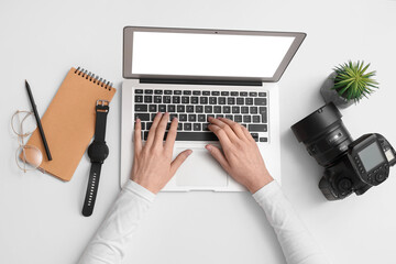 Female hands with modern laptop, professional photo camera, smartwatch and notebook on light background
