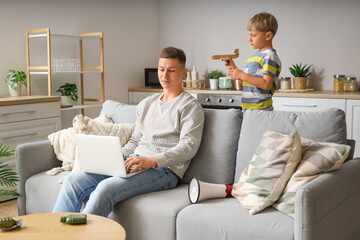 Little boy playing with toy airplane and his working father at home
