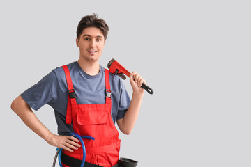 Male plumber with pipe wrench and hoses on grey background