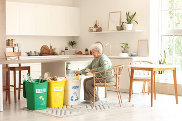 Senior woman with notebook and garbage bins in kitchen. Waste sorting concept