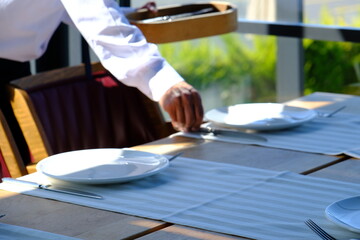 Dinner preparations in luxury restaurant. Forks and knives, serving plates. Waiters preparing tables for customers. Dining table and chair, Bosphorus view. White tablecloths. Service industry.