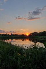 Sunset over the river with the reflection of the sky in the water. A peaceful rural atmosphere. Sunset in a summer village over a lake with a church in the distance.