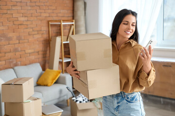 Beautiful woman with cardboard boxes and mobile phone in room on moving day