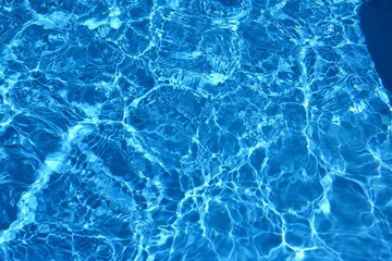 Blue rippling water surface in swimming pool under sunlight, abstract aquatic background with light reflections.