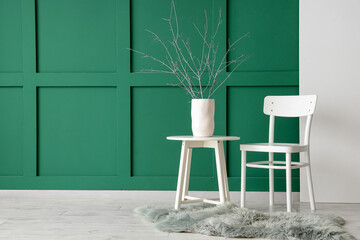 Chair and tree branches in vase on coffee table near green wall with canvas