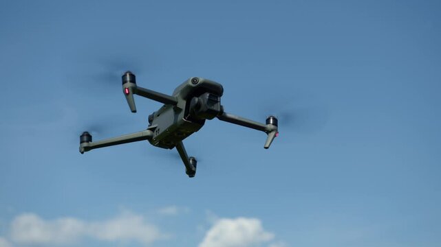 A drone soars through the clear blue sky, showcasing picturesque views of an expansive landscape below. The sun illuminates the scenery, enhancing the vibrant colors.