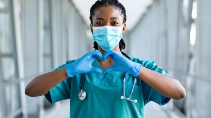 Dedicated African American female doctor making heart gesture wearing mask and scrubs - Powered by Adobe
