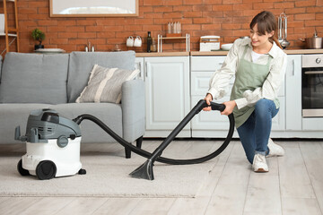 Pretty young woman with vacuum cleaner cleaning carpet at home
