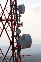 Tall red lattice communication tower holds multiple large round microwave antennas and dishes, set...