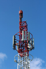 Red and white steel telecommunications tower with multiple antennas and dishes stands tall against a deep blue sky, supporting mobile and radio signal transmission in a modern network