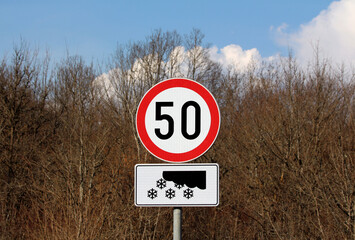 Circular speed limit 50 sign with red border stands above a snow warning symbol, set against...