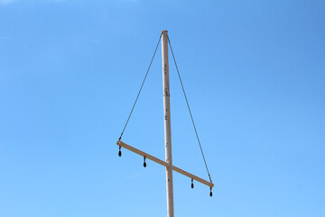 Tall white metal sailboat mast with horizontal spar and five pulleys stands against a clear blue...