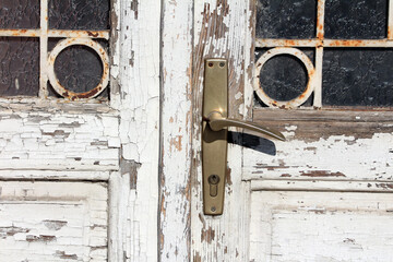 Close-up of an old white wooden door with peeling paint, brass handle, and stained glass panels...