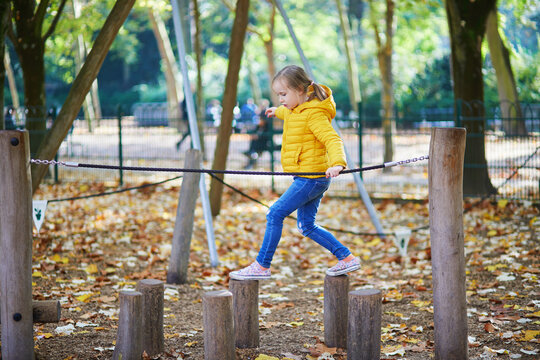 Cheerful little girl having fun on playground in autumn park in Paris, France.