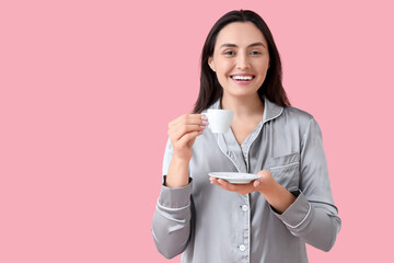 Young woman in pajamas with cup of coffee on pink background