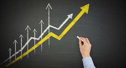 Hand drawing upward trending graph on chalkboard
