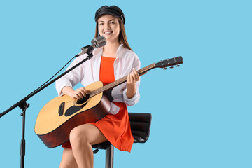Young woman with microphone and guitar singing on blue background