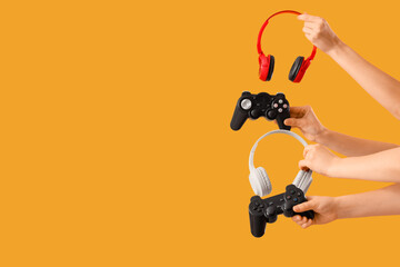 Female hands with game pads and headphones on yellow background