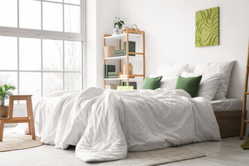 Cozy bed, bookcase and houseplant on stand in interior of bedroom