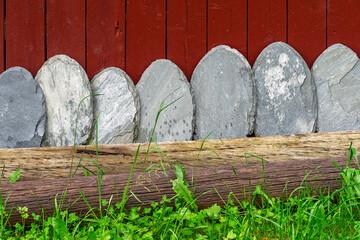 A series of smooth, oval-shaped stones lines the base of a red wooden fence, surrounded by lush...