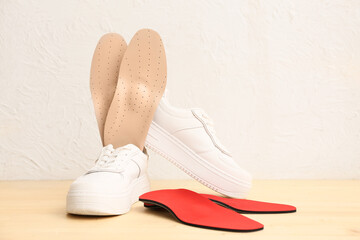 Sneakers with orthopedic insoles on wooden table near light wall