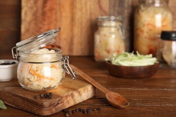 Tasty sauerkraut in jar with condiments on wooden table. Closeup