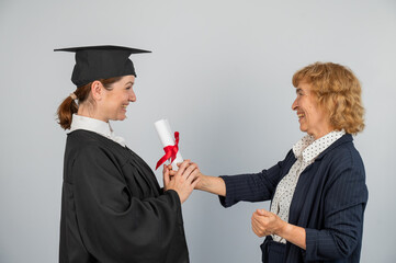 An elderly Caucasian woman presents a diploma to a graduate. 