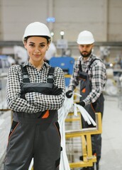 Portrait of confident female factory worker with male colleague transporting materials in background
