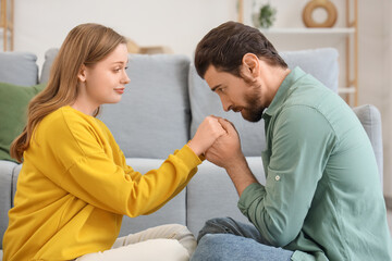 Apologizing young man holding his wife's hands at home
