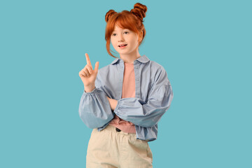 Teenage redhead girl pointing at something on blue background