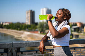 Portrait of young sporty African woman in sportswear drinking energy drink while enjoying taking a...
