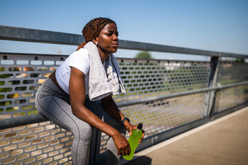 Portrait of tired African woman with sweat on her face resting after exercising and drinking energy...