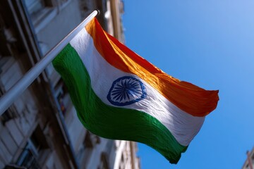 Indian flag waving against blue sky attached to a pole buildings blurred in the background