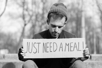 Homeless man holding cardboard with text JUST NEED A MEAL on street