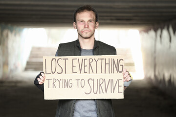 Homeless man holding cardboard with text LOST EVERYTHING TRYING TO SURVIVE on street