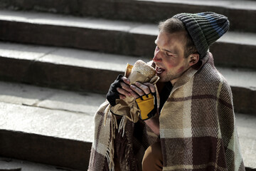 Homeless man with plaid eating bread on street