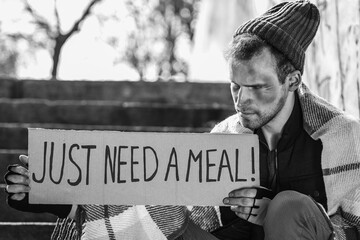 Homeless man holding cardboard with text JUST NEED A MEAL on street