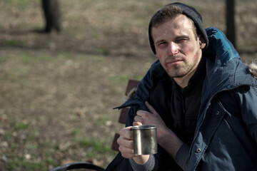 Frozen homeless man with cup begging for money in park